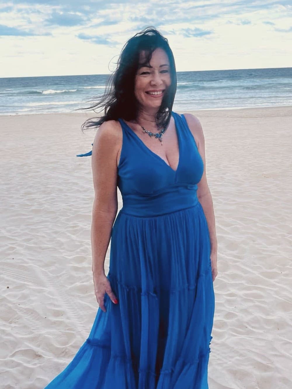 Sindy, the artist, smiling on a windswept beach in a blue dress